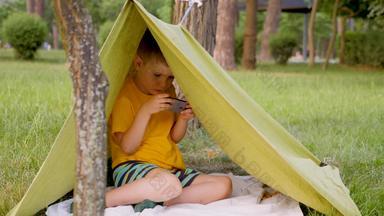 年轻的旅行者帐篷玩视频游戏旅行概念男孩手使帐篷戏剧游戏移动孩子自然小工具